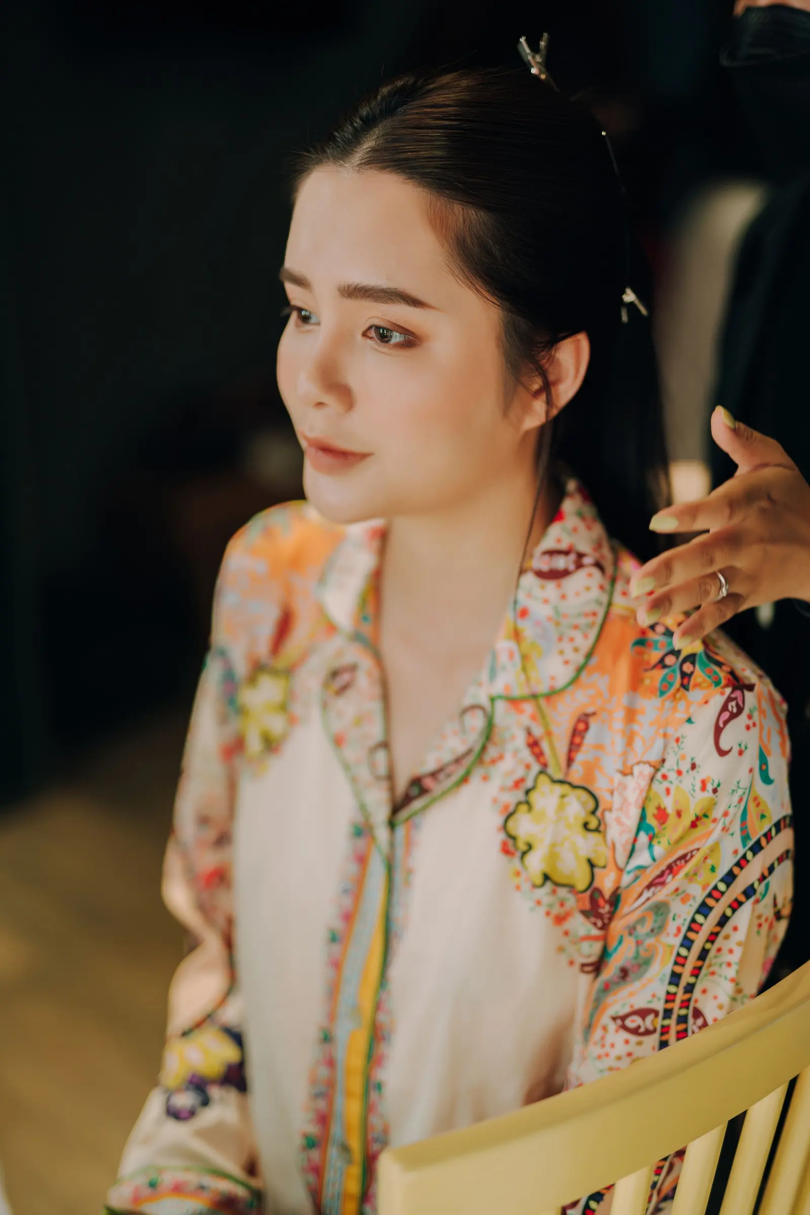 A woman in a patterned robe looking away while her makeup is finished