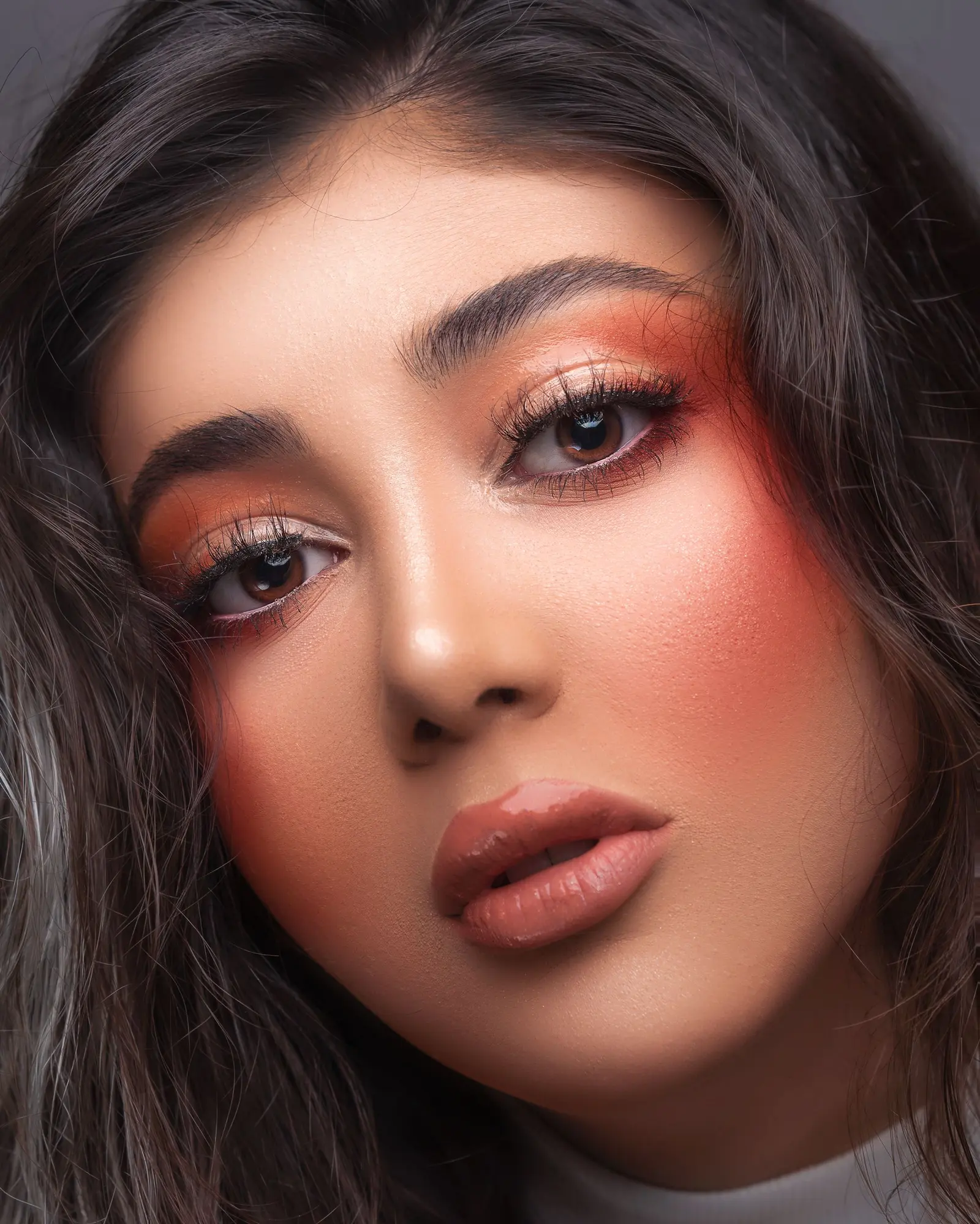 A woman with warm coral blush and soft eyeshadow looking into the camera