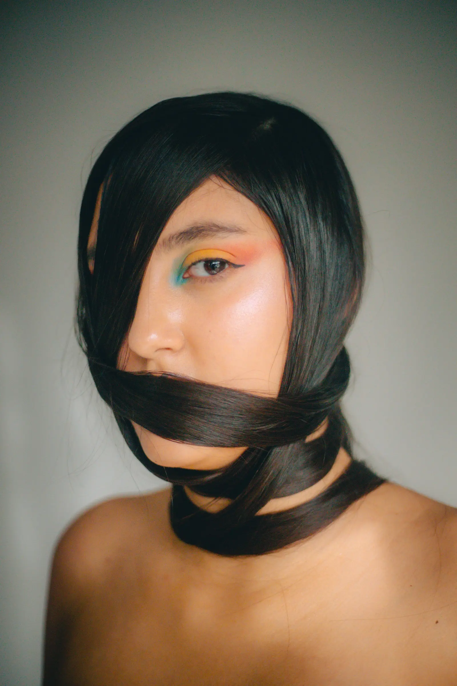 A woman with a sleek black bob wrapped across her face and teal eyeshadow