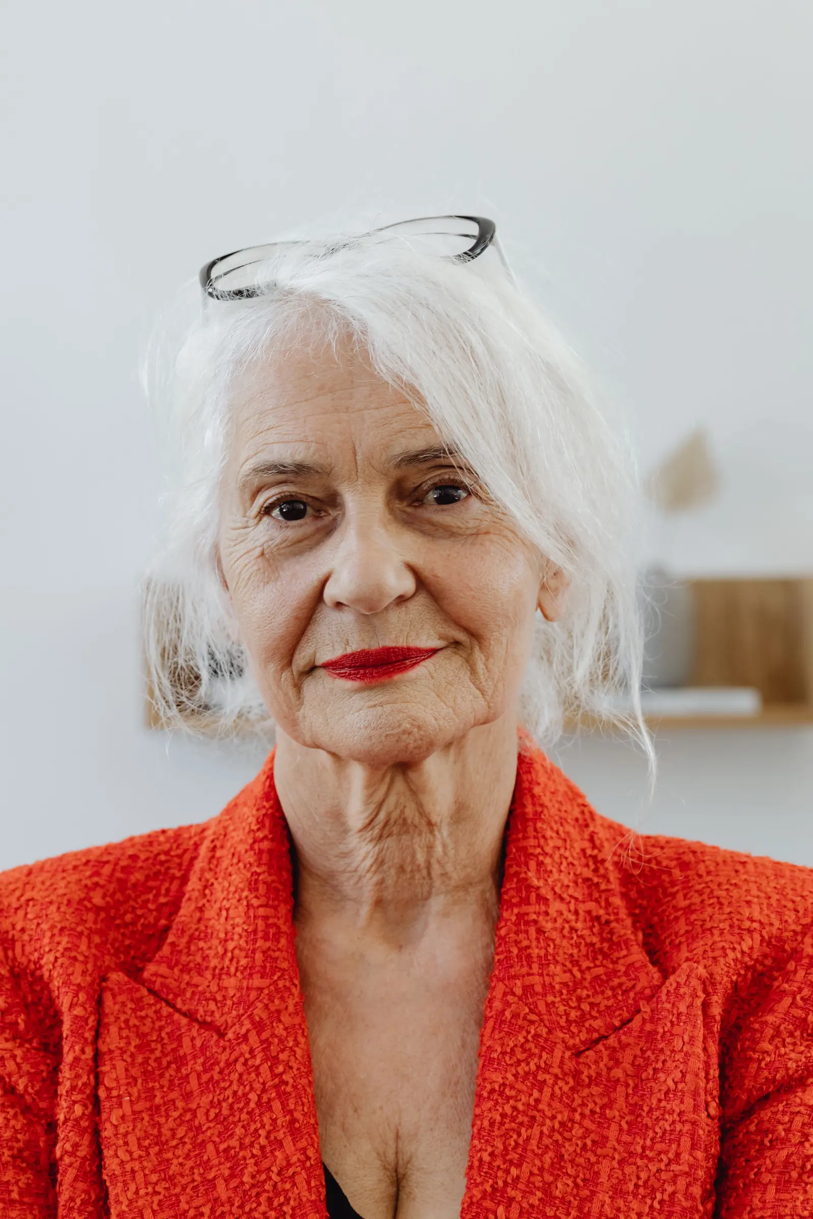 A silver-haired woman in an orange blazer and red lipstick