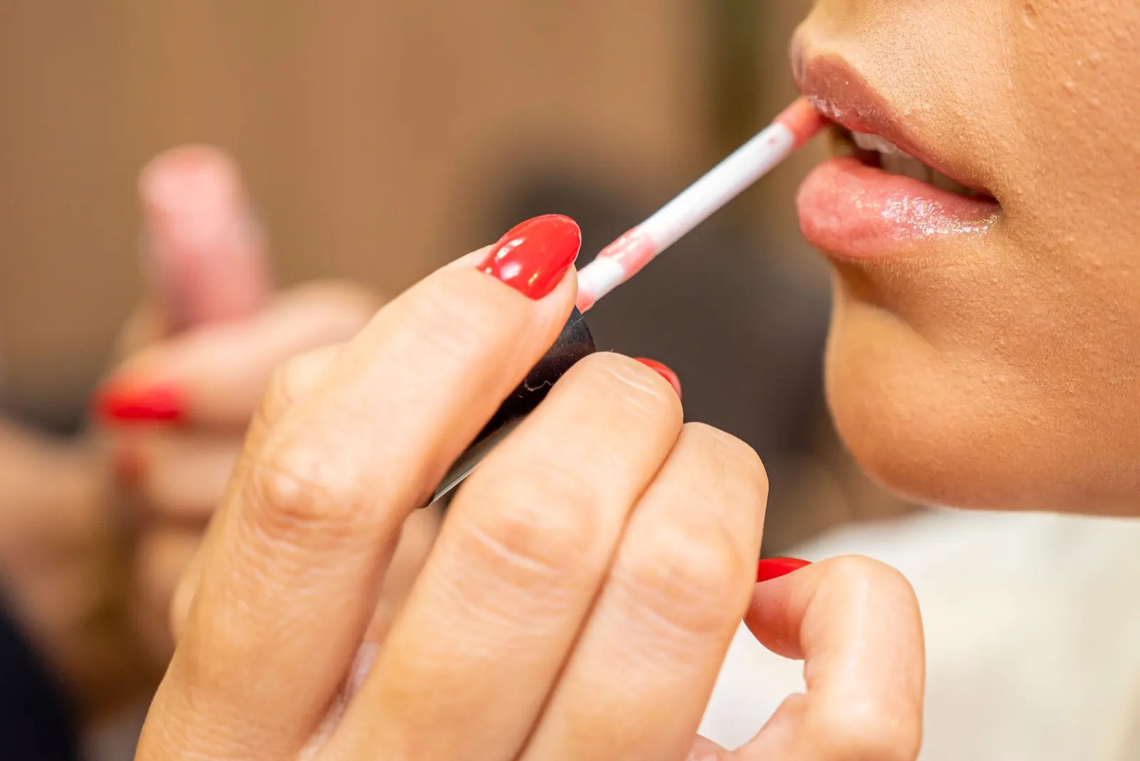 A gloss applicator touching a woman's lips, her fingertips painted red
