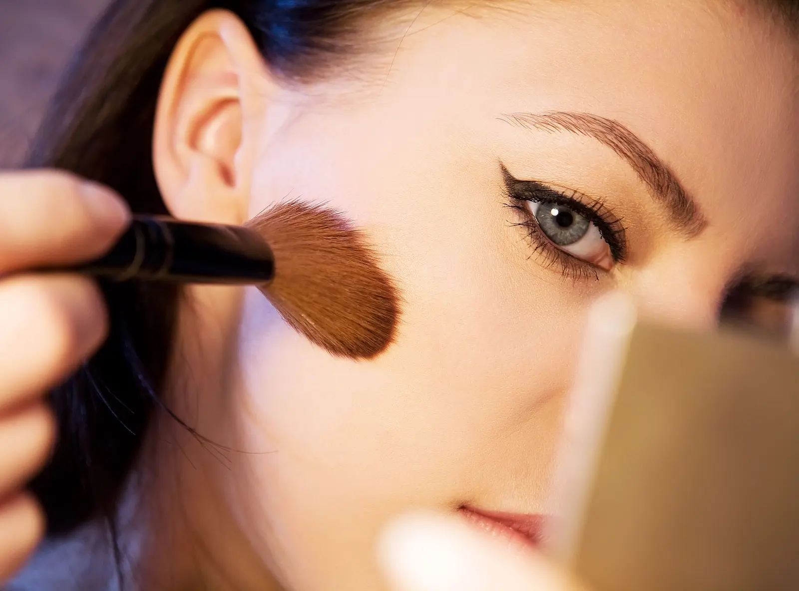 A makeup brush sweeping peach blush across a cheek